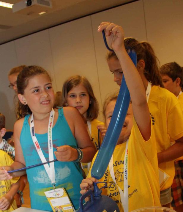 Mehrere Kinder pumpen Luft in einen blauen Ballon.