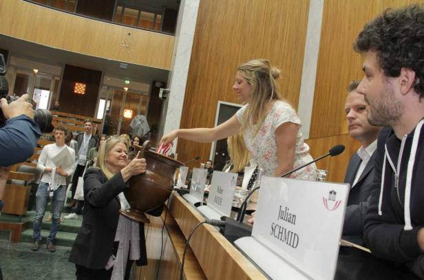 Zwei Frauen hantieren mit einer großen Urne in einem formellen Rahmen.