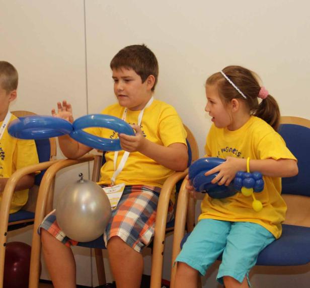 Kinder sitzen auf Stühlen und formen blaue Luftballons.