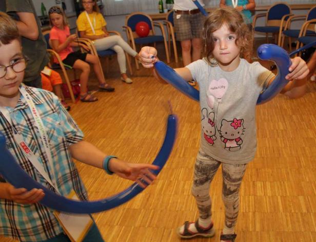 Ein Mädchen und ein Junge formen blaue Luftballons zu Figuren.