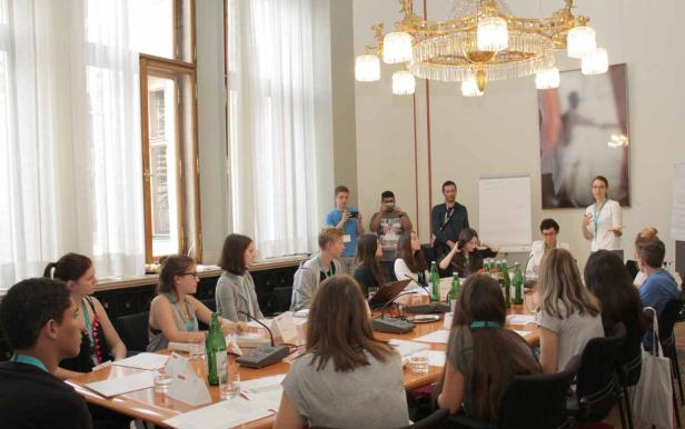 Eine Gruppe junger Leute sitzt an einem Tisch während einer Präsentation in einem Konferenzraum.