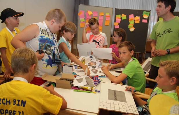 Eine Gruppe Kinder arbeitet an einem Tisch mit Papier, Scheren und Stiften an einem Projekt.