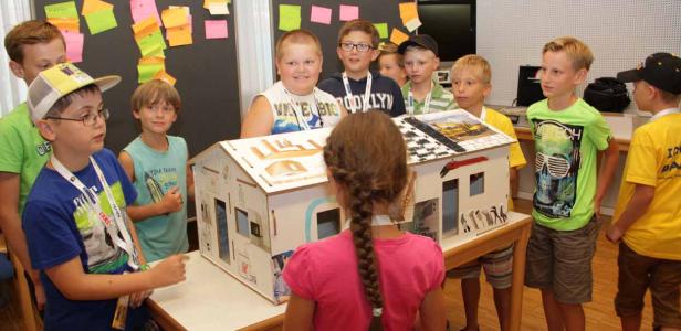 Eine Gruppe von Kindern betrachtet ein Modellhaus auf einem Tisch.
