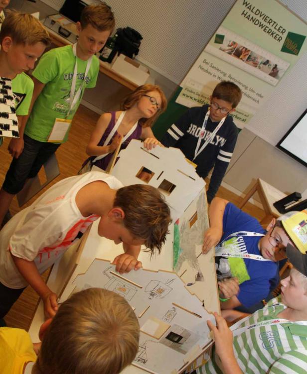 Eine Gruppe Kinder arbeitet an einem Modellhaus aus Pappe.