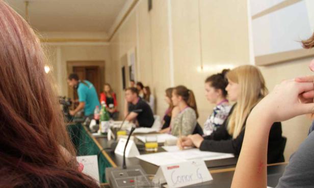 Mehrere Personen sitzen an einem Tisch während einer Konferenz oder eines Seminars.