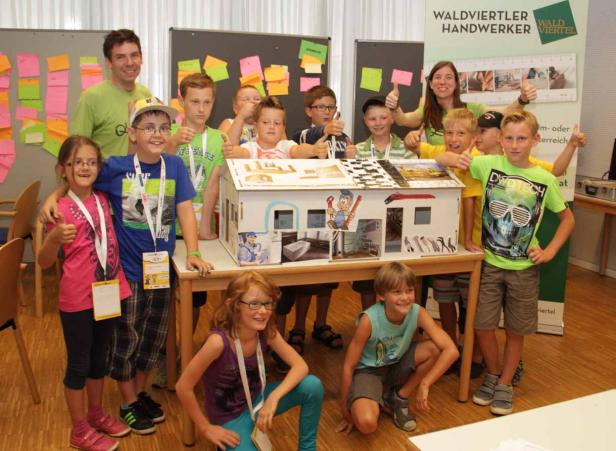 Eine Gruppe Kinder präsentiert stolz ein Modellhaus mit Handwerker-Motiven.