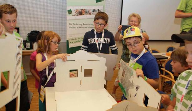 Kinder bauen ein Modellhaus aus Pappe zusammen.