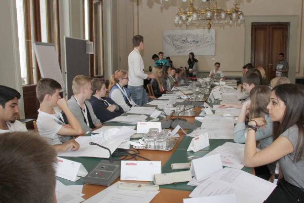 Eine Gruppe junger Leute sitzt an einem langen Tisch in einem Konferenzraum.