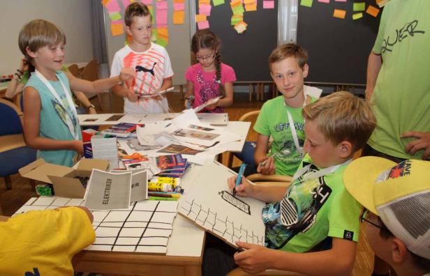 Eine Gruppe Kinder sitzt an einem Tisch und bastelt mit Papier und Stiften.