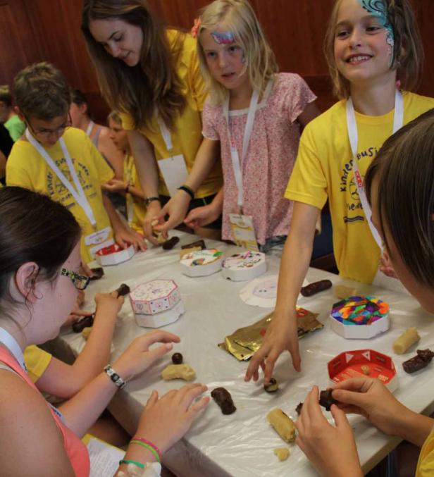 Kinder und eine Betreuerin formen Figuren aus Marzipan an einem Tisch.