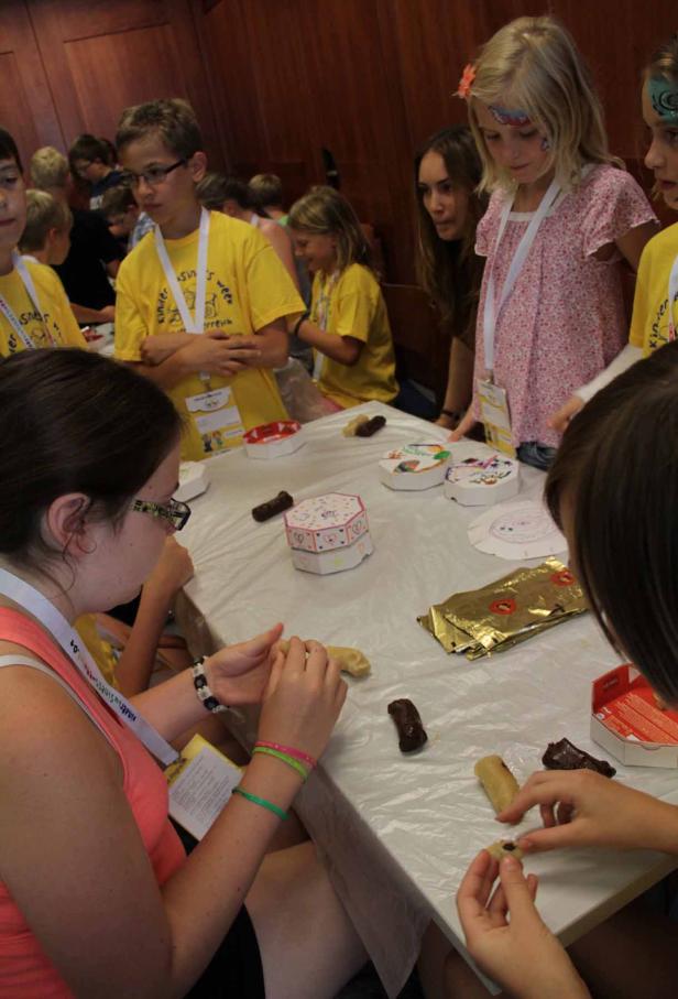 Kinder sitzen an einem Tisch und formen Marzipankartoffeln.