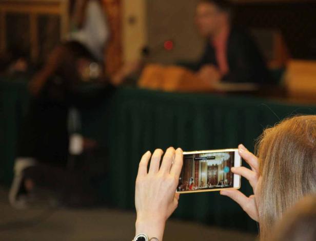 Eine Frau filmt mit ihrem Smartphone eine Veranstaltung in einem eleganten Saal.