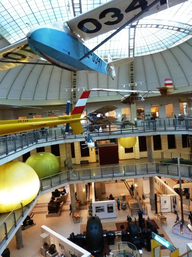 Verschiedene Flugzeuge und ein Hubschrauber hängen in einem Museum unter einer Glaskuppel.