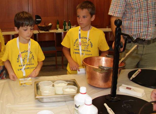 Zwei Jungen in gelben T-Shirts stehen an einem Tisch mit Käseutensilien.