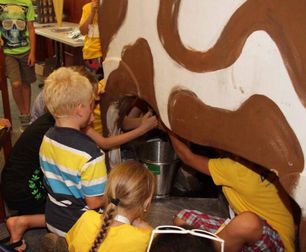 Kinder melken eine bemalte Kuhattrappe.