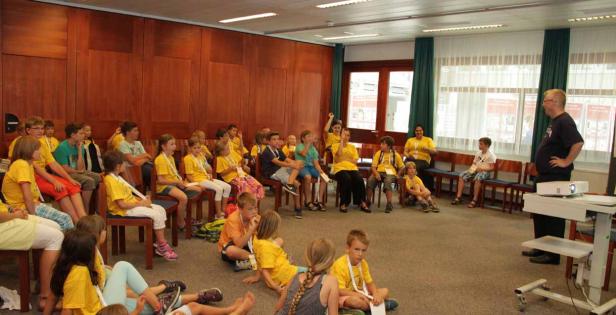 Eine Gruppe Kinder sitzt in einem Raum und hört einem Mann bei einer Präsentation zu.