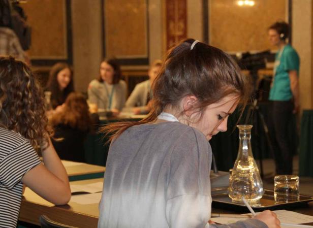 Eine junge Frau sitzt an einem Tisch und schreibt etwas auf ein Blatt Papier.