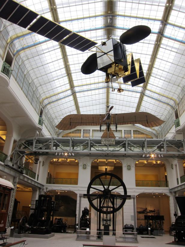 Ausstellungsraum mit einem Satellitenmodell und einem historischen Flugzeug unter einem Glasdach.