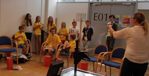 Eine Gruppe Kinder und eine Frau stehen in einem Raum mit der Aufschrift E01.