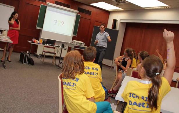 Kinder sitzen in einem Raum und hören einem Vortrag zu.