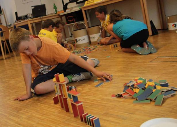 Kinder spielen mit bunten Holzbausteinen auf einem Holzboden.