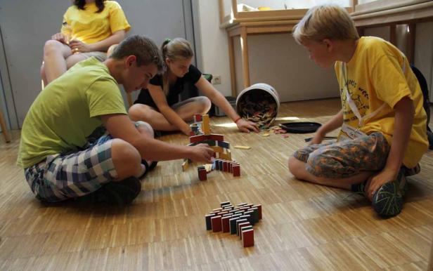 Drei Kinder sitzen auf dem Boden und spielen mit Dominosteinen.