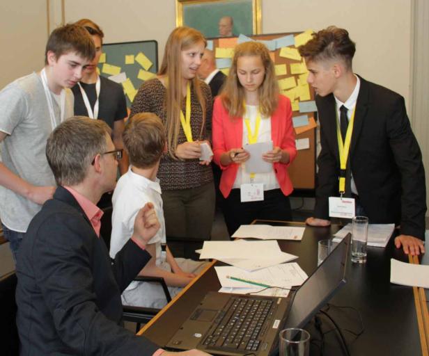 Eine Gruppe junger Leute arbeitet mit einem Mann an einem Tisch mit einem Laptop und Papieren.