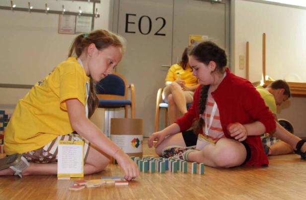 Zwei Mädchen sitzen auf dem Boden und spielen mit Dominosteinen.