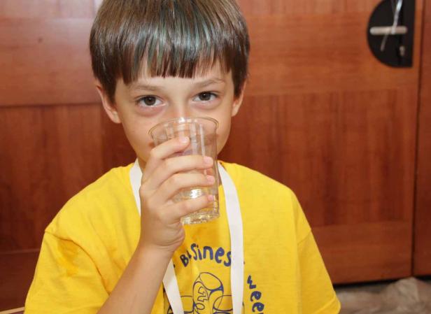Ein Junge im gelben T-Shirt trinkt aus einem durchsichtigen Plastikbecher.