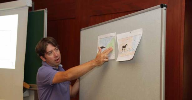Ein Mann präsentiert Zeichnungen von Pferden an einer Tafel.