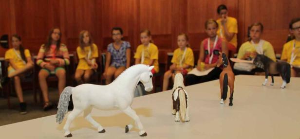 Eine Gruppe von Mädchen betrachtet Modellpferde auf einem Tisch.