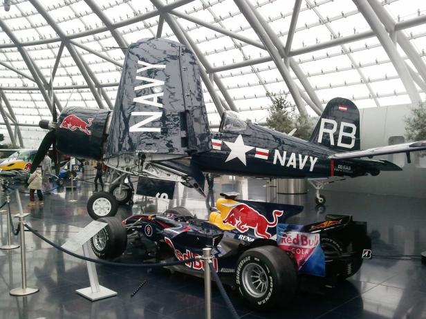 Eine F4U-4 Corsair der US Navy und ein Formel-1-Wagen von Red Bull in einer Ausstellung.