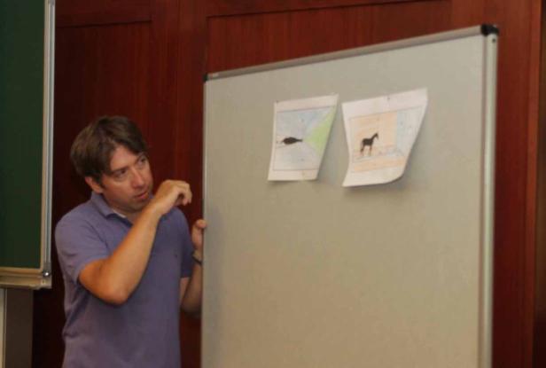 Ein Mann steht vor einer Tafel mit Zeichnungen eines Fisches und eines Pferdes.