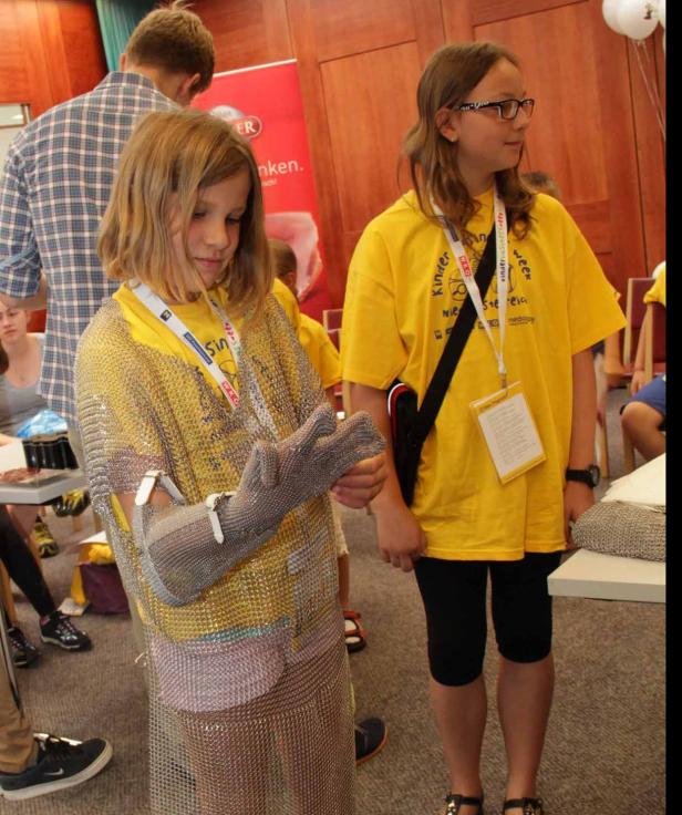 Ein Mädchen probiert ein Kettenhemd an, während ein anderes Mädchen daneben steht.