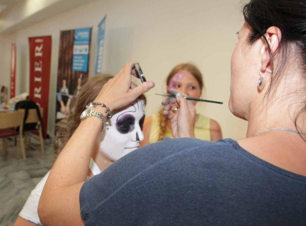 Eine Frau schminkt einer anderen Frau das Gesicht im Stil von „Dia de los Muertos“.