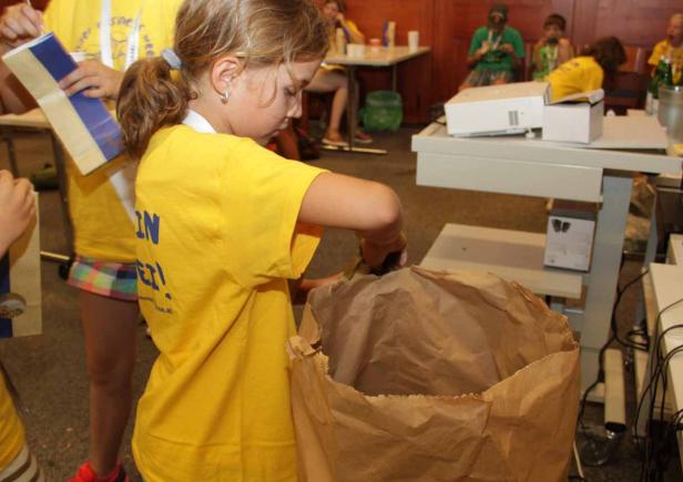 Ein junges Mädchen mit gelbem T-Shirt befüllt eine große Papiertüte.