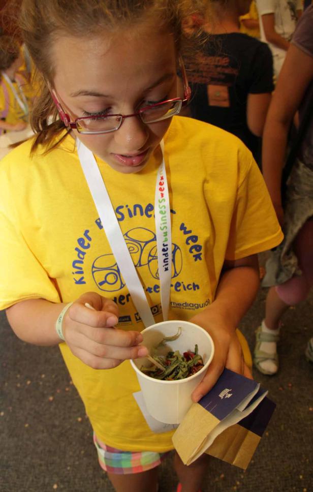 Ein Mädchen mit Brille betrachtet eine Mischung aus Kräutern und Gewürzen in einem Becher.