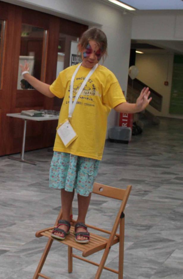 Ein Mädchen mit Gesichtsbemalung steht auf einem Stuhl und balanciert.