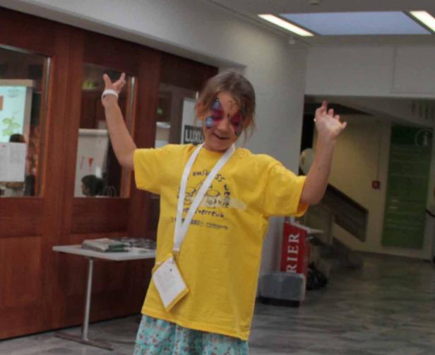 Ein Mädchen mit Schmetterlingsgesichtsbemalung und gelbem T-Shirt steht mit erhobenen Armen da.