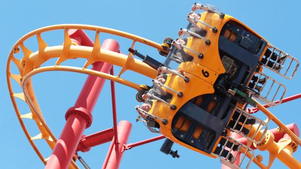 Menschen fahren mit einer gelben Achterbahn mit rotem Gestell.