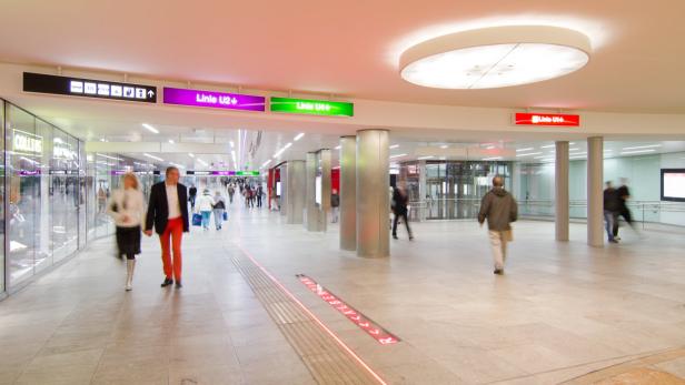 Menschen gehen in einer U-Bahn-Station mit Geschäften und Wegweisern.