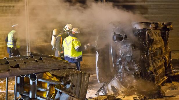 Polizei und Feuerwehrleute untersuchen ein ausgebranntes Autowrack.