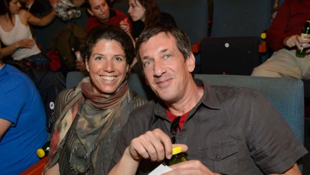 Ein lächelndes Paar sitzt im Publikum, der Mann öffnet eine Flasche.