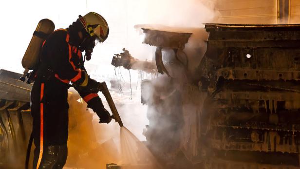 Ein Feuerwehrmann löscht ein brennendes Objekt mit einem Wasserstrahl.
