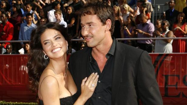 Adriana Lima und ihr Begleiter posieren lächelnd vor einer Menschenmenge.