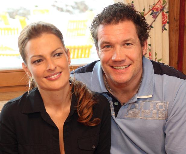 Ein lächelndes Paar sitzt nebeneinander vor einem Fenster.