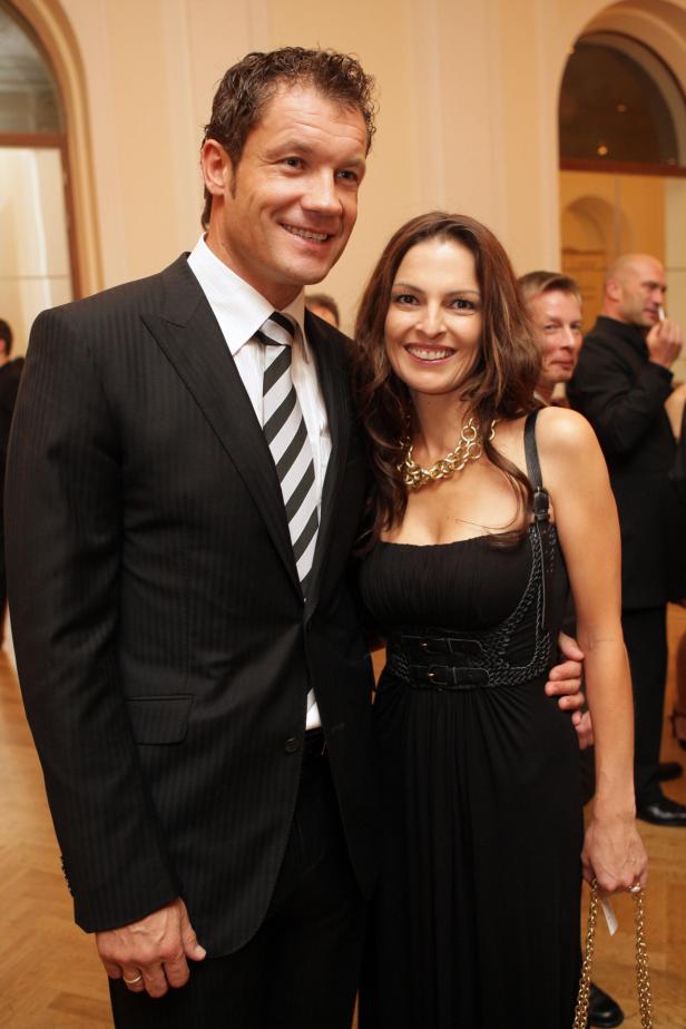 Ein Mann im Anzug und eine Frau im schwarzen Kleid posieren lächelnd.