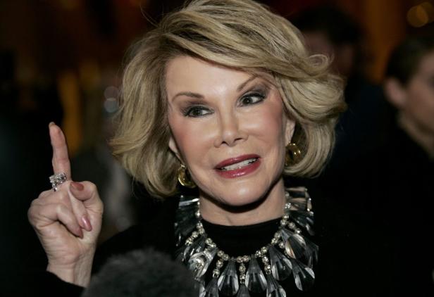 Joan Rivers mit erhobenem Zeigefinger und auffälligem Schmuck.