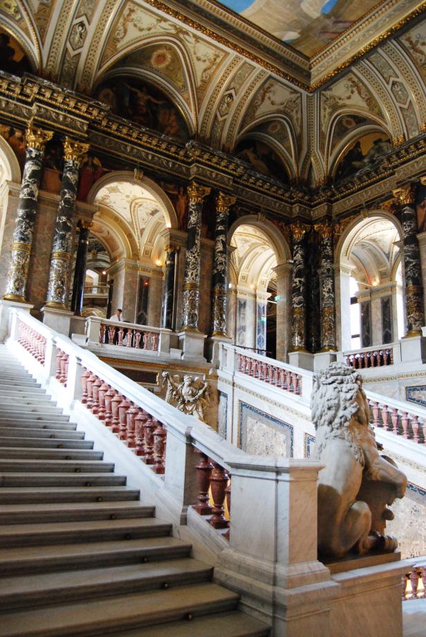 Eine prunkvolle Treppe mit Marmorstufen und einer Löwenstatue in einem opulenten Gebäude.