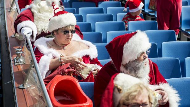 Mehrere als Weihnachtsmänner verkleidete Menschen sitzen auf blauen Sitzen.